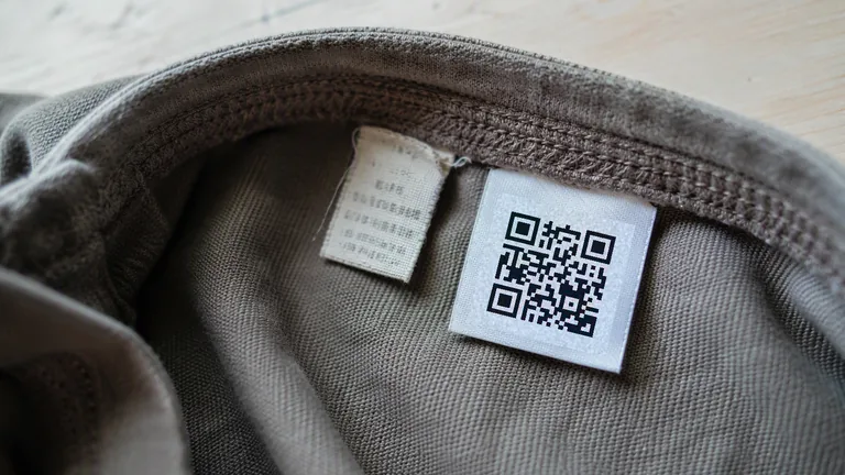 A woven QR code tag stitched into the inside neck of a cotton garment, next to the printed care label