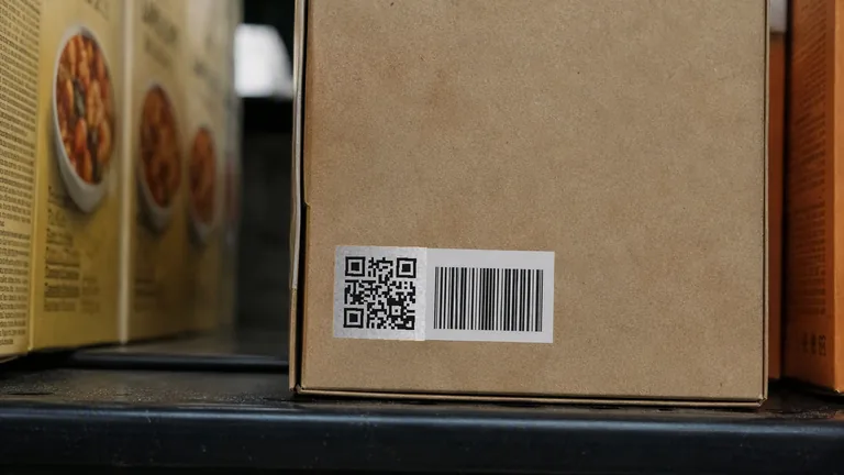 The back of a plain cardboard food carton on a supermarket shelf, carrying a printed label with a QR code beside a barcode