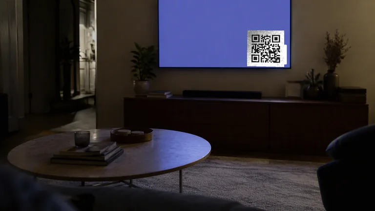A wall mounted television in a darkened living room showing an advertisement with a QR code in the corner of the screen
